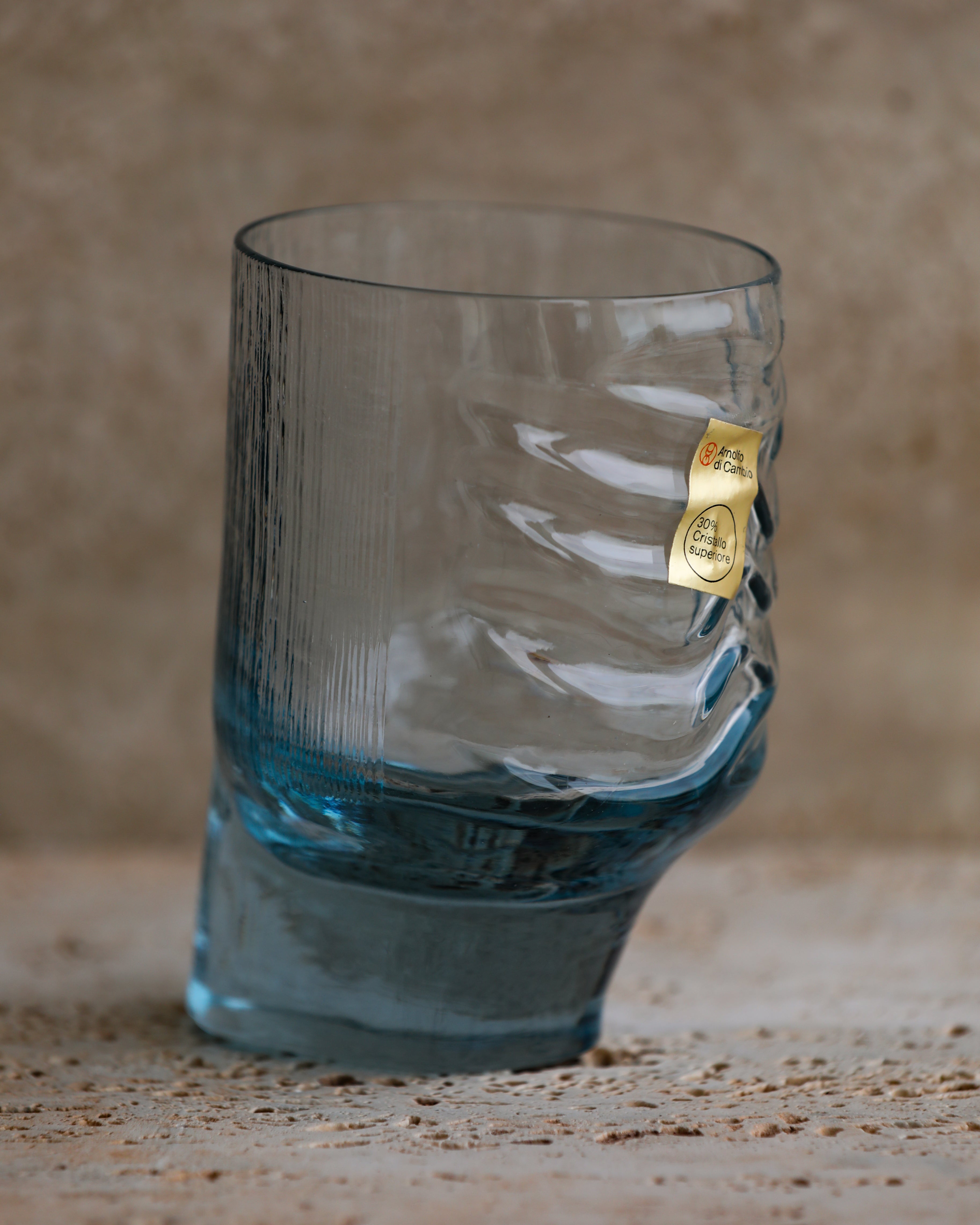 Close-up of cobalt blue sculpted tumbler glass showing textured wave design and original Arnolfo di Cambio label.