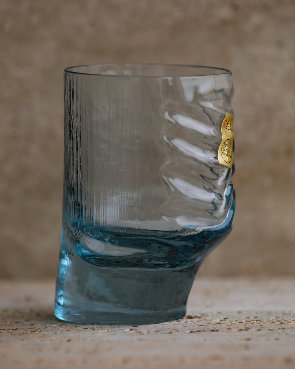 Side view of sculpted cobalt blue tumbler highlighting asymmetrical form and textured glass.
