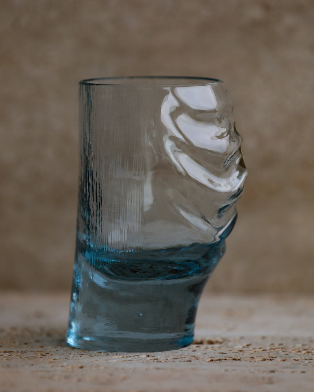 Profile view of cobalt blue sculpted glass tumbler with swirling wave details.