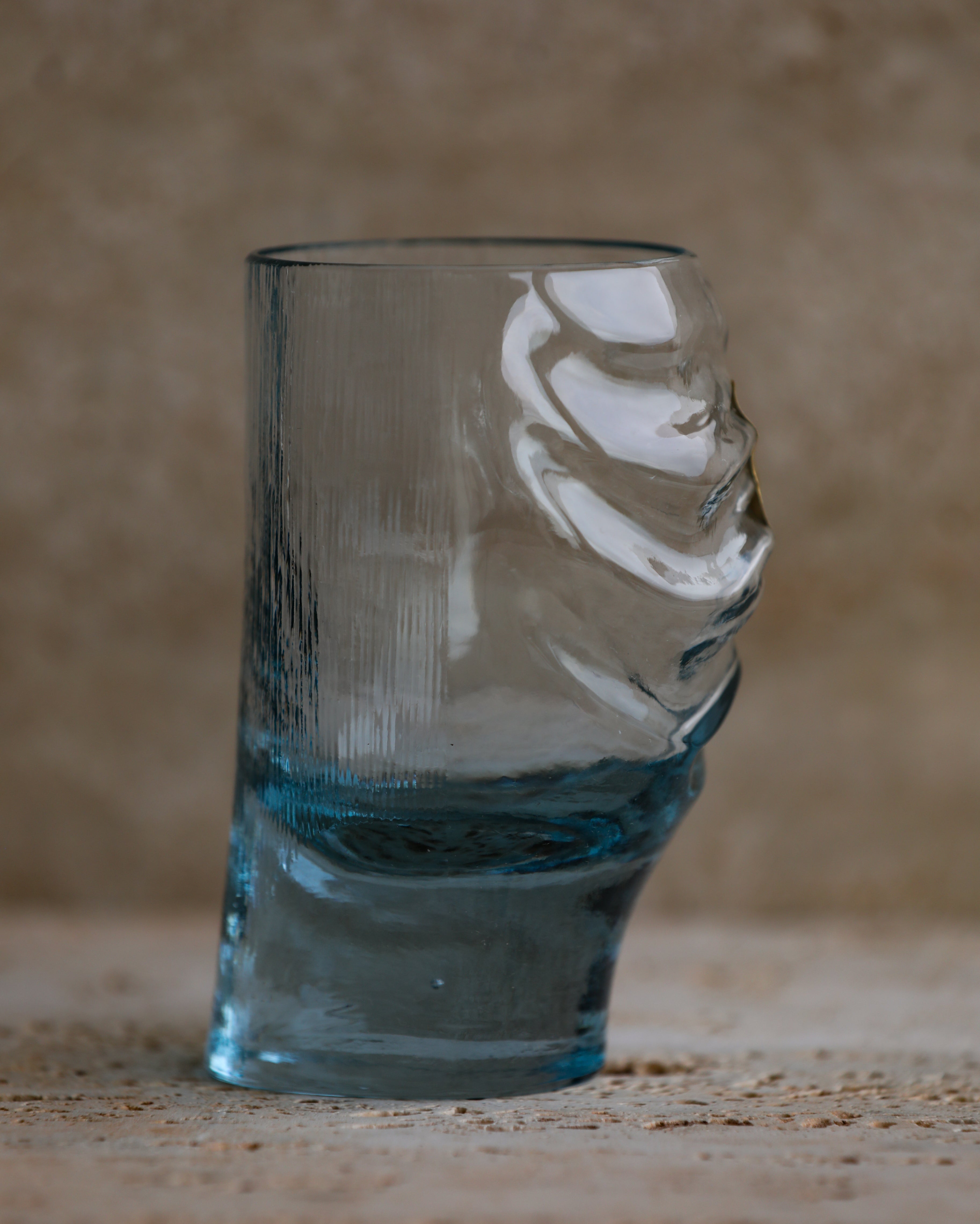 Profile view of cobalt blue sculpted glass tumbler with swirling wave details.
